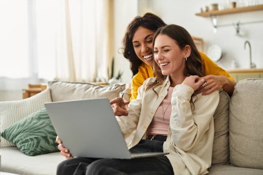 Evde iki kadın, sıcaklıkla çevrili bir laptopu paylaşırken birlikte gülüp gülümsüyor..