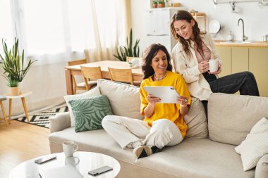 İki kadın rahat bir kanepede rahatlar, tableti incelerken keyifli bir anı paylaşırlar..