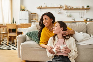 İki kadın, rahatça uzanırken, birbirlerine eşlik ederken şefkatli bir şekilde gülümserler..