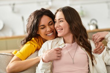 İki kadın, evlerinde birbirlerini kucaklayarak, odayı aydınlatan gülümsemelerini paylaşırlar..