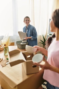 İki kadın yeni evlerinde kutuları açarken gülüşlerini ve gülüşlerini paylaşıyorlar..