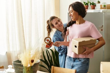 İki kadın sevinçle kutuları açıyor ve evlerinde birbirlerine eşlik ederek eğleniyorlar..