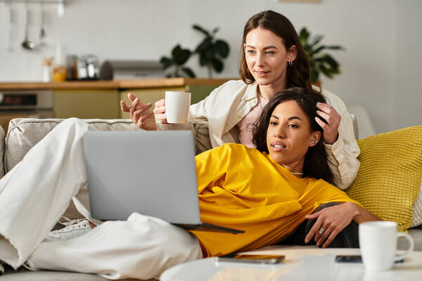 Loving couple relaxes at home, sharing laughter and connection over a laptop while enjoying drinks.