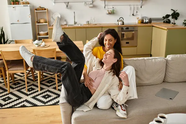 İki kadın, sıcak ve davetkar bir ev ortamıyla çevrili bir kanepede neşeyle kucaklaşır..