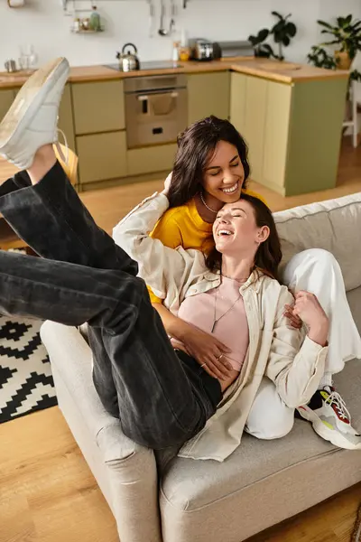 İki kadın, lüks yaşam alanlarında rahat bir kanepede kahkaha ve neşe paylaşıyor..