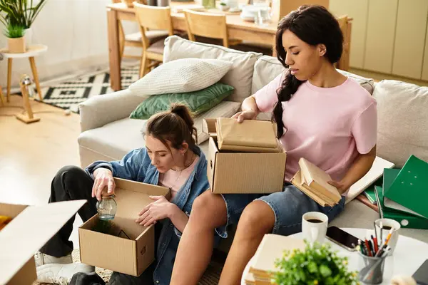 İki kadın kutularını açıyor, yeni evlerine yerleşirken birbirlerine eşlik ediyorlar..