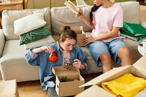 İki kadın, rahat oturma odalarındaki hazine paketlerini açarken gülümsüyor..