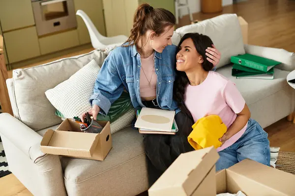 İki kadın sıcak ve davetkar oturma odalarında kutuları açarken sevgiyle sarılıyorlar..