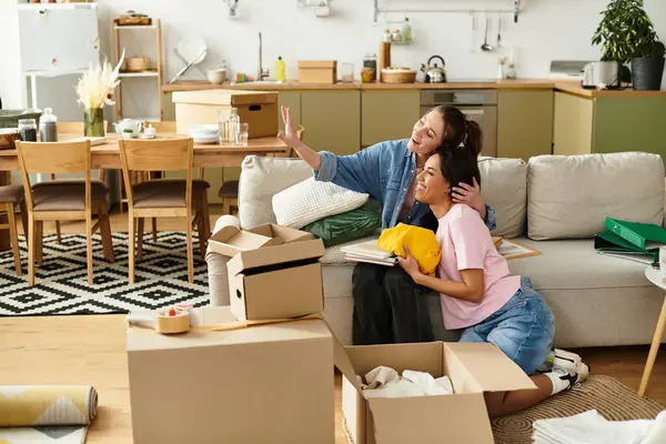 Kutularla çevrili rahat yaşam alanlarında yerleşirken iki kadın mutlu mesut kucaklaşır..