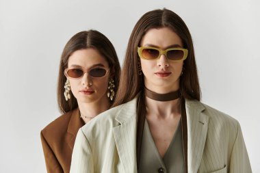 Uzun saçlı ve şık güneş gözlüklü iki güzel kadın zarif bir şekilde poz veriyor..