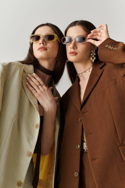 İkiz kardeşler modaya uygun kıyafetlerini ve son moda güneş gözlüklerini sergilerken güven saçıyorlar.