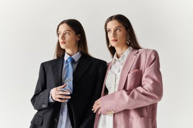 İkiz kardeşler, parlak bir stüdyoda birlikte poz verirken büyük beden takım elbiseler içinde zarafet sergilerler..