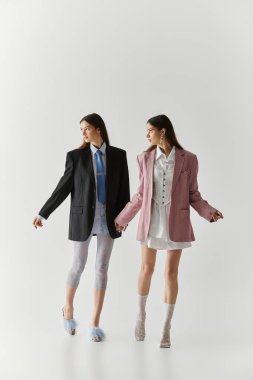 Güzel genç ikiz kardeşler modern bir stüdyo ortamında el ele tutuşurken tarzlarını ifade ederler..