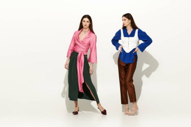 İkiz kardeşler canlı bir arkaplan karşısında şık kıyafetler içinde güzellik ve tarz yayarlar..