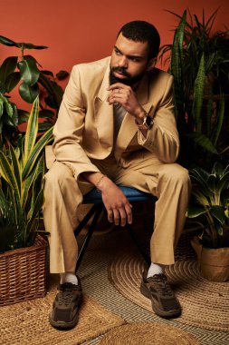 Genç bir adam, rahat bir ortamda canlı bitkiler arasında otururken yaz modasını sergiliyor..