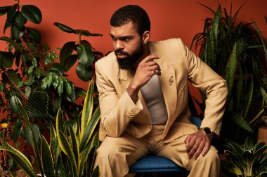 Kendine güveni tam bir genç adam şık bir yaz elbisesi giyer ve kapalı alanda yemyeşil yapraklarla etkileşime girer..