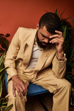 Hafif takım elbiseli genç ve yakışıklı bir adam çiçeklerin arasında düşünceli bir şekilde oturuyor..