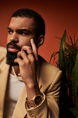 Yakışıklı adam yemyeşil ortamda düşünceli bir şekilde poz veriyor, yaz modasını ve cazibesini sergiliyor..