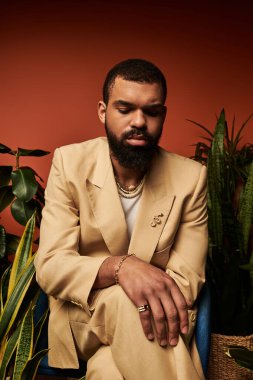 Açık bej takım elbiseli bir adam yemyeşil bitkilerin arasında gevşer ve yaz havası yayar..