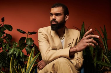 Tarz sahibi genç bir adam yaz estetiğinde canlı bitkilerin arasında oturarak kendine güven yayar..