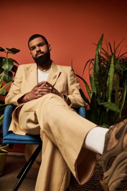 Şık bir genç adam, bereketli bitkiler ve yaz atmosferiyle çevrili mavi bir sandalyede rahatlar..