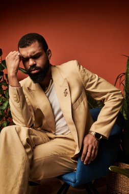 Bej takım elbiseli yakışıklı genç adam rahat bir sandalyede rahatlar ve hayatı düşünür..
