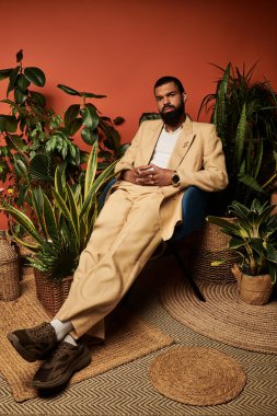 Zarif bir genç adam gösterişli yaz moda atmosferleri sergilenen yeşilliklerin arasında şık bir şekilde oturuyor..