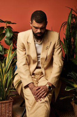 Hafif takım elbiseli yakışıklı genç bir adam çevrende canlı bitkilerle oturuyor..