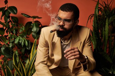 Yaz kıyafetli yakışıklı adam puro içerken etrafını canlı bitkilerle sarar..