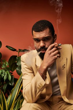 Tarz sahibi genç bir adam yaz cazibesini kucaklarken sigara içiyor ve günün tadını çıkarıyor..