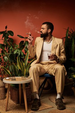 Şık bir genç adam, bereketli yeşilliklerle çevriliyken yaz modasına uygun bir içkiyle rahatlar..