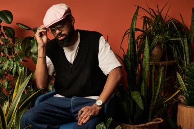 Genç bir adam, canlı iç mekan bitkilerinin arasında yaz stili sergiliyor, büyüleyici cazibe ve güven saçıyor..