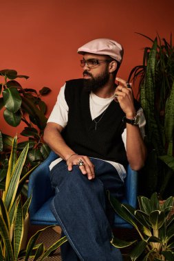 Yakışıklı bir adam, yaz modasına uygun giyinmiş, kendine güvenen, yemyeşil bir yerde oturuyor..