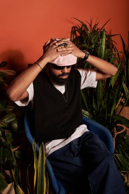 Şık bir genç adam modern bir sandalyede gevşeyip bereketli bitkilerle dolu bir yaz estetiğini sergiliyor..