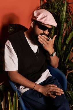 Yakışıklı genç bir adam rahat bir sandalyede rahatlar, hayat dolu bir arkaplana karşı bir cazibe yayar..