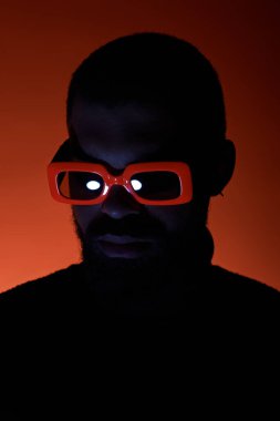 Genç bir adam canlı bir yaz arkaplanının ortasında cesur turuncu gözlüklerini sergiliyor..