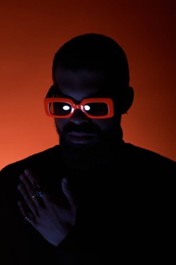 Genç bir adam çarpıcı bir arka plana karşı cesur güneş gözlükleriyle canlı bir yaz modası sergiliyor..