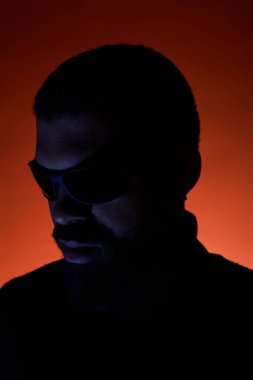 Genç bir adam sıcak aydınlatma altında koyu güneş gözlükleriyle yaz modasına modellik yapıyor..