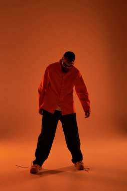 Yakışıklı bir adam, son moda yaz kıyafetlerini giyip, sıcak turuncu bir arka planda cazibesini sergiliyor..