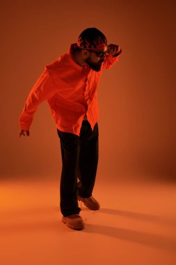 Turuncu gömlekli ve güneş gözlüklü genç bir adam renkli bir atmosferde tarzını ifade ediyor..