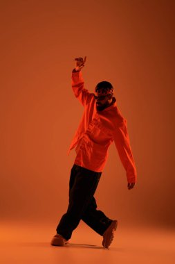 Genç adam, yumuşak turuncu ışık altında şık bir yaz elbisesi içinde güven içinde dans ediyor..