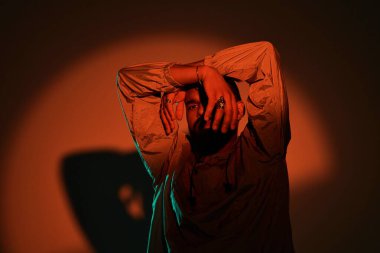 Yakışıklı genç bir adam, sanatsal ışıklandırma ile dramatik bir şekilde poz verirken şık bir yaz tarzı sergiliyor..