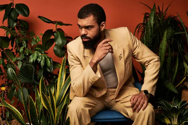 Kendine güveni tam bir genç adam şık bir yaz elbisesi giyer ve kapalı alanda yemyeşil yapraklarla etkileşime girer..