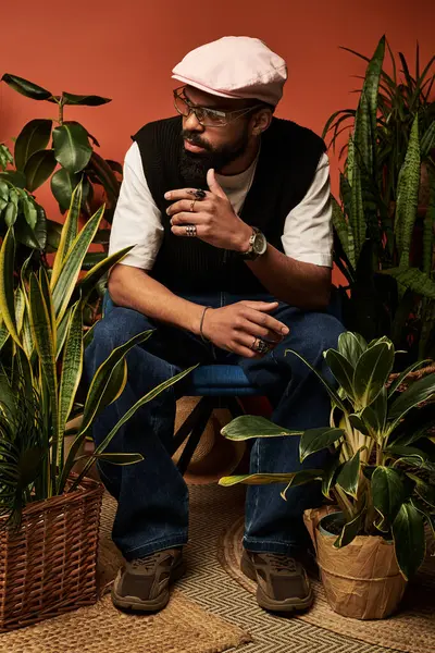 Şık bir genç adam rahat bir şekilde çeşitli bitkilerin arasında oturur, rahat bir yaz havasını somutlaştırır..