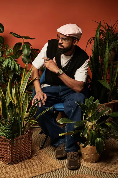 Şık giyinmiş yakışıklı bir adam, bir dizi iç mekan bitkisinin arasında oturur ve yaz havası yayar..