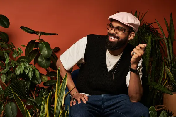 Şık yaz kıyafetleri içinde genç bir adam sıcak bir alanda renkli bitkilerle çevrili gülümsüyor..