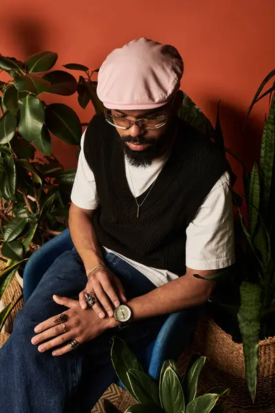 Minimalist giyinmiş genç bir adam, bitkilerin arasında saatine hayran bir şekilde sakin bir anın tadını çıkarıyor..