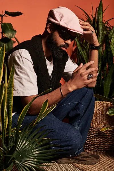 Sakallı ve güneş gözlüklü genç adam, bitkilerin arasında dinlenirken yaz estetiği yayıyor..