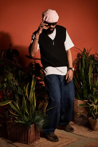 Genç adam yaz havası yayıyor, şık giyinmiş, canlı bitkiler ve turuncu arka planla çevrili..