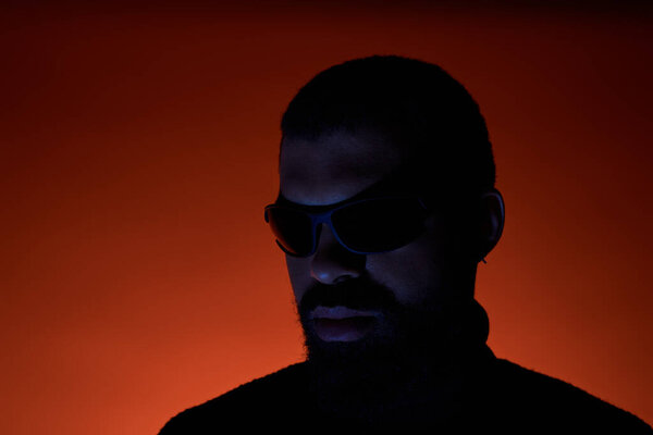 Стильный молодой человек с бородой и солнцезащитными очками уверенно выглядит в яркой летней обстановке.